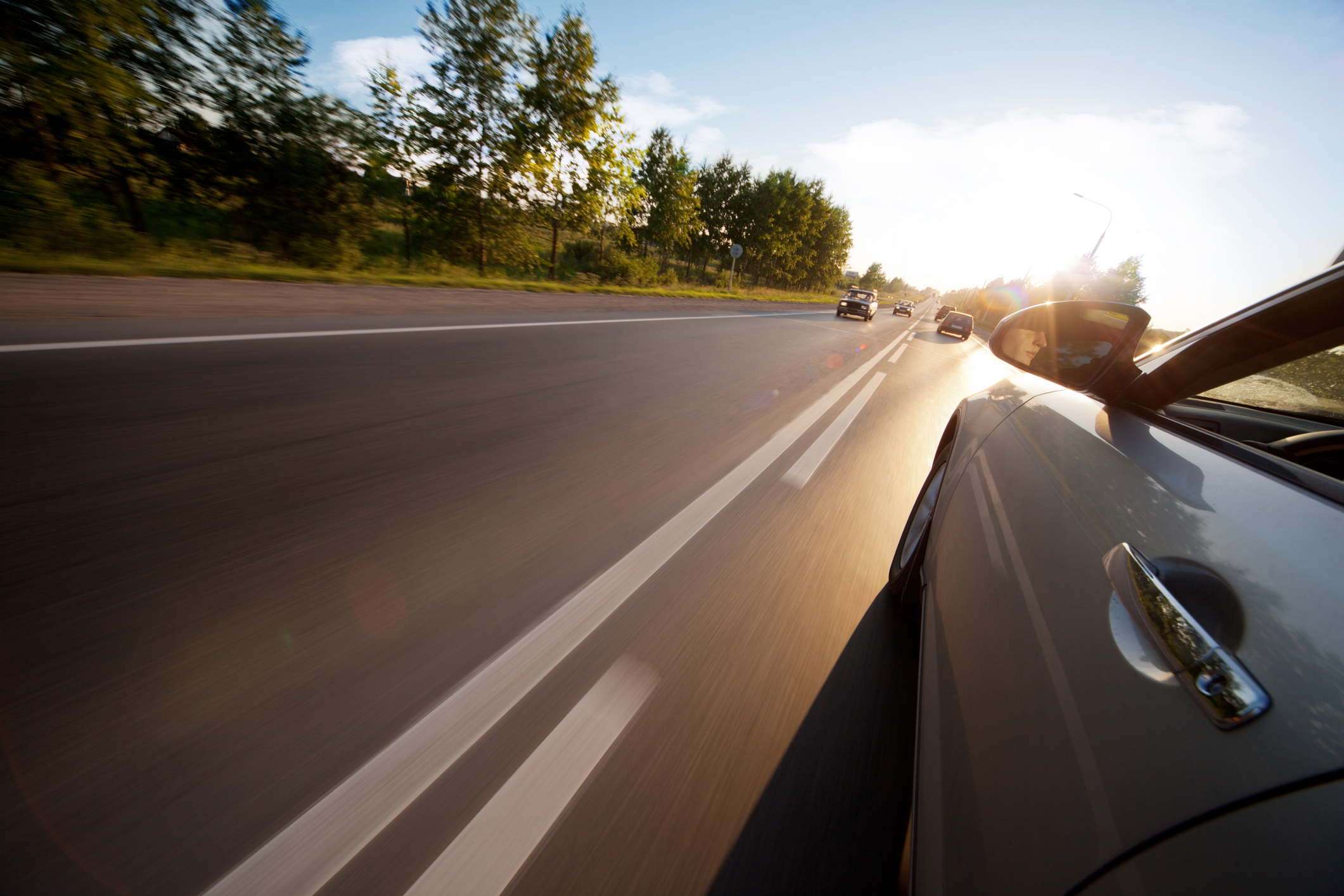 Side view of a car driving down a 2 lane road on a sunny day.